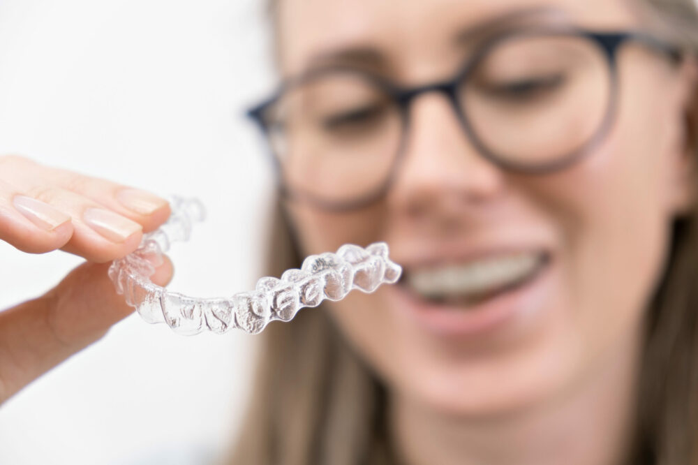 smiling woman using clear plastic removable braces aligner or whitening tray. dental orthodontic care.