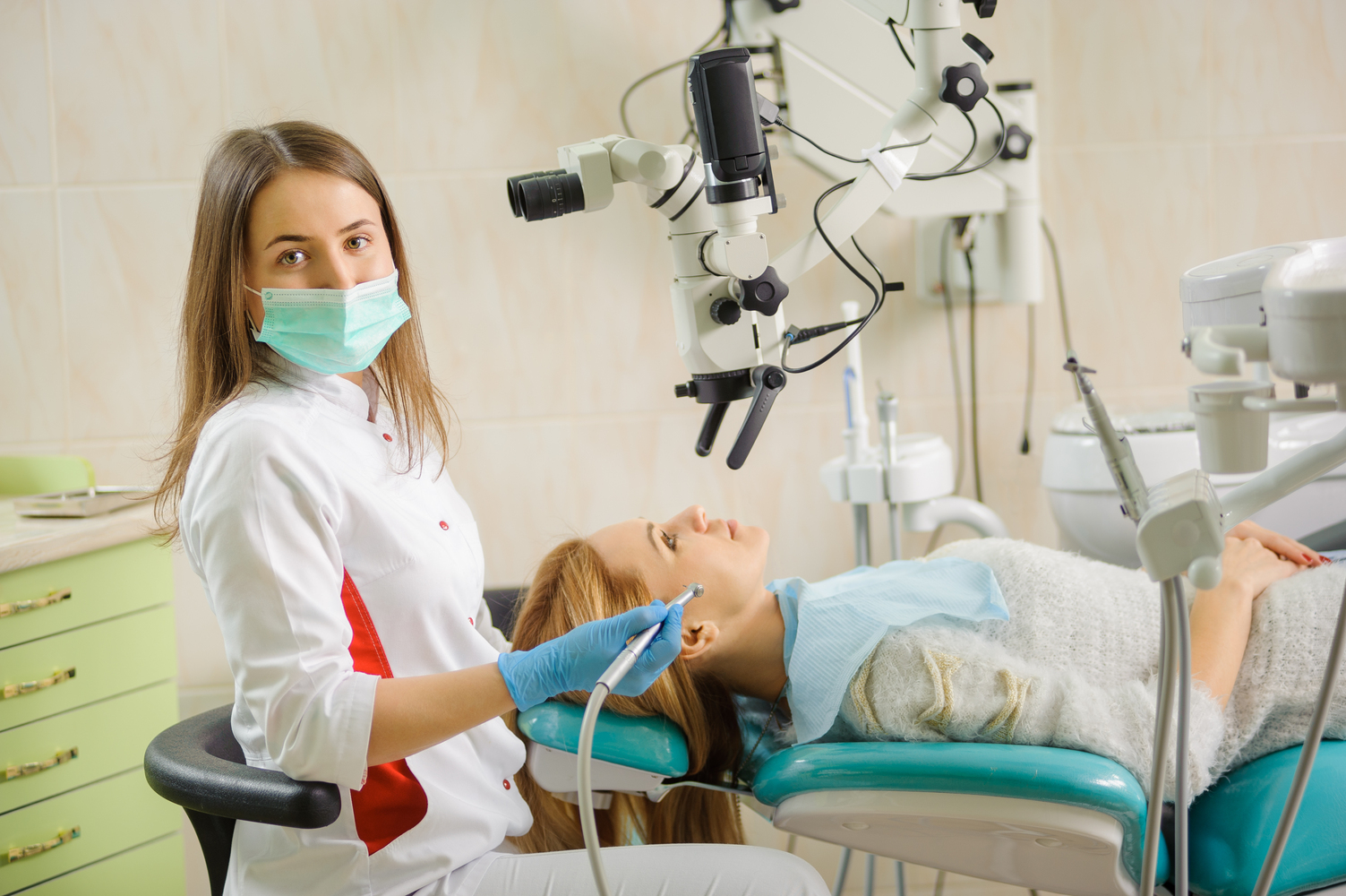 Portrait of beautiful female dentist treating caries using microscope at the hospital, dentist smiling and looking at the camera. Dental care and treatment.