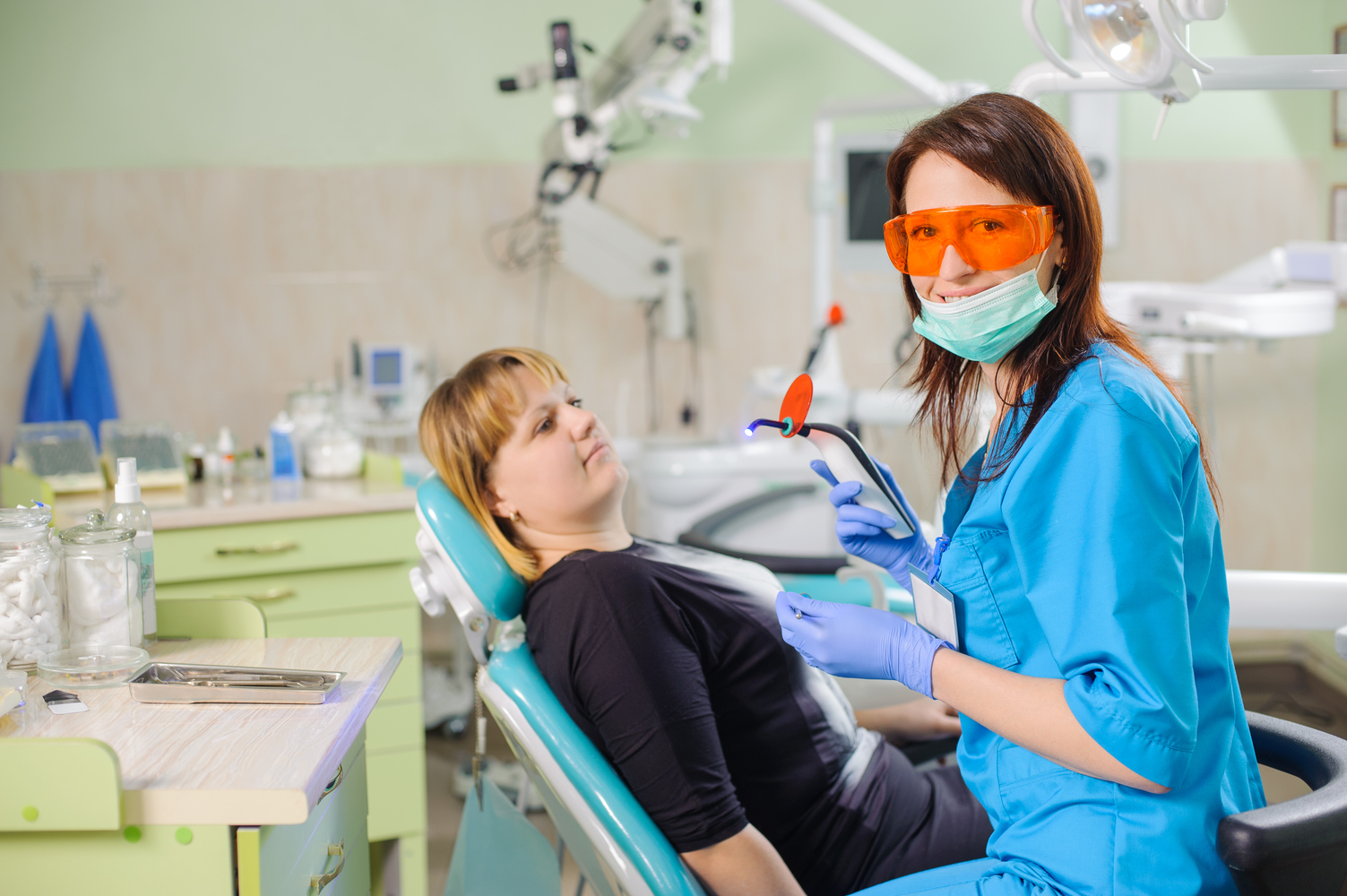 Female dentist doctor is holding dentist photopolymer lamp getting ready to treat patient in clinic. Woman is wearing gloves and glasses. Medical equipment. Dental care and treatment