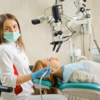 Portrait of beautiful female dentist treating caries using microscope at the hospital, dentist smiling and looking at the camera. Dental care and treatment.