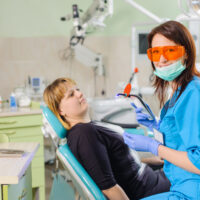 Female dentist doctor is holding dentist photopolymer lamp getting ready to treat patient in clinic. Woman is wearing gloves and glasses. Medical equipment. Dental care and treatment