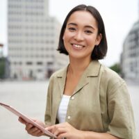 young-smiling-asia-woman-with-tablet-standing-on-2022-12-14-03-57-13-utc (1)